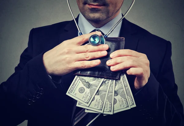 Бизнесмен со стетоскопом слушает бумажник с долларовыми купюрами — стоковое фото