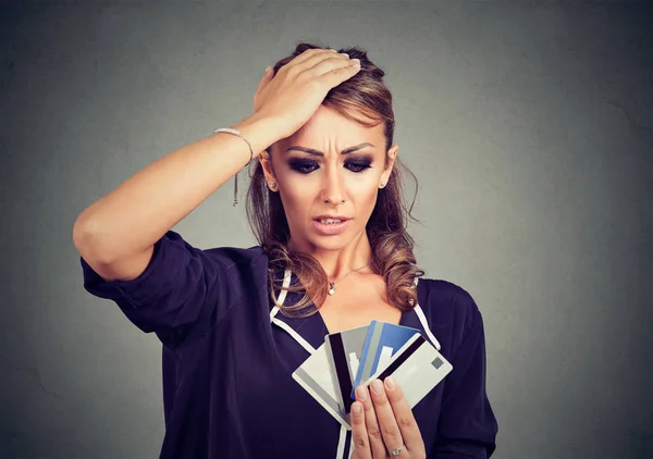Запутавшаяся молодая женщина смотрит на слишком много кредитных карт — стоковое фото