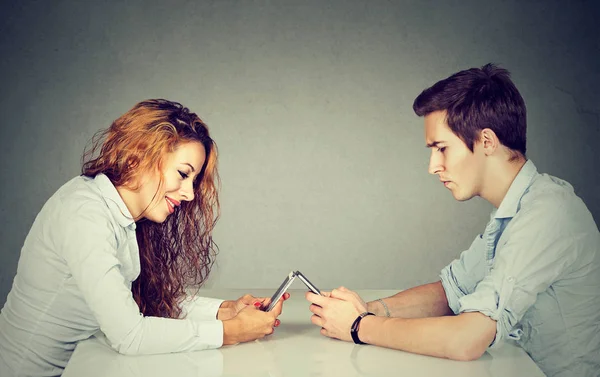 Concepto de adicción a teléfonos inteligentes. Mujer y hombre sentados en la mesa con el teléfono inteligente ignorándose mutuamente — Foto de Stock