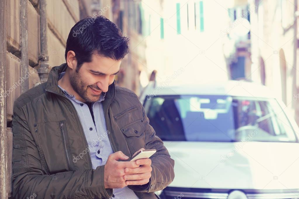 Successful young man standing by his car texting on mobile phone 