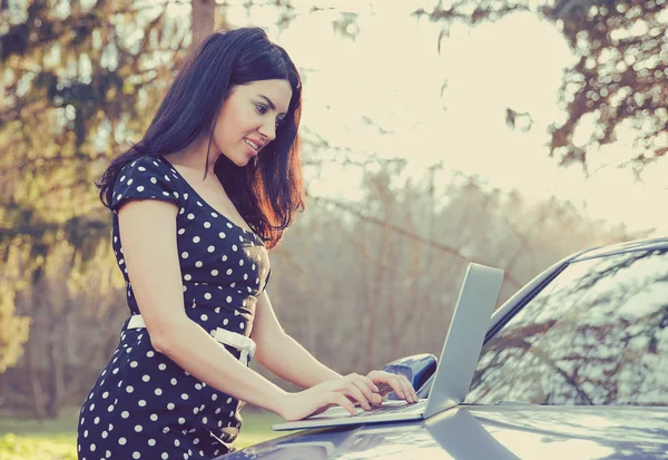 Lachende vrouw met behulp van computer laptop buiten staande door haar auto — Stockfoto