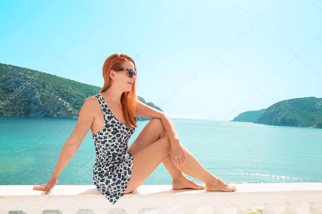 Woman looking at sea view. Young lady living fancy jetset lifestyle wearing dress on holidays. Amazing view of seaside and islands 