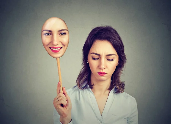 Sad young woman looking down taking off happy mask of herself — Stock Photo, Image