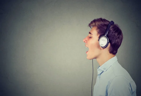 Stilig kille med hörlurar i blå skjorta lyssnar på musik och sång — Stockfoto