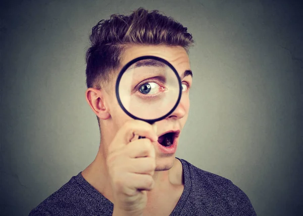 Curious young man looking through a magnifying glass — Stock Photo, Image