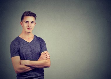 Duvar arka plan karşı dururken raslantı yakışıklı kendine güvenen erkek t-shirt tutma kollarında geçti