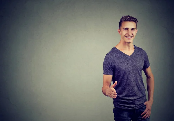 Smiling man in t-shirt holds out his hand for a handshake and looking at the camera — Stock Photo, Image