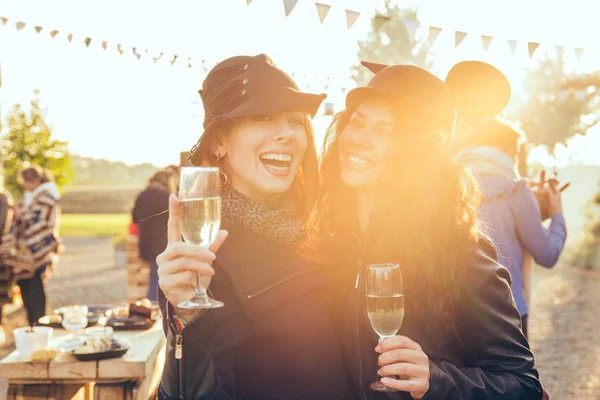 Две счастливые девушки на улице пьют белое вино и веселятся в сельской местности. — стоковое фото