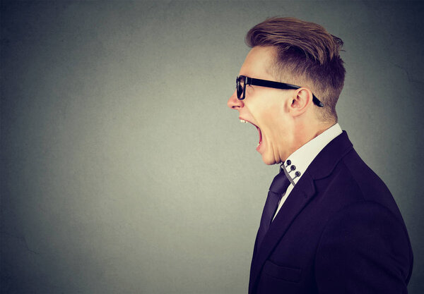 Side profile portrait of an angry young business man screaming 