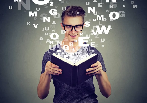 Homem feliz lendo um livro com letras alfabéticas voando para cima do livro — Fotografia de Stock