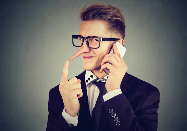 Ravasz fiatalember beszél a mobiltelefon hosszú orr. Hazug koncepció. — Stock Fotó