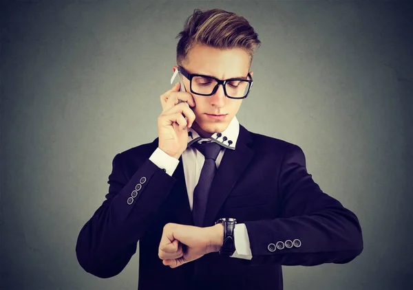 Businessman looking at wrist watch, talking on mobile phone. — Stock Photo, Image