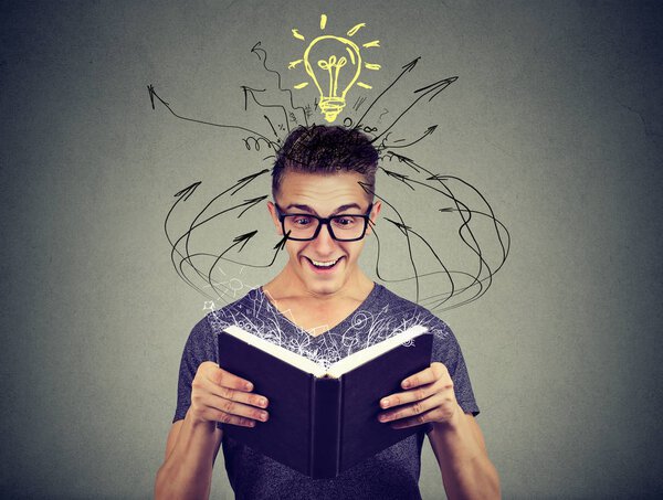 Счастливый молодой человек читает книгу с лампочкой над головой
 