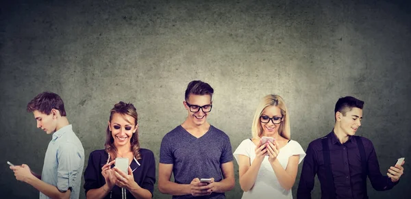 Young casual people using mobile phone standing together against concrete wall — Stock Photo, Image