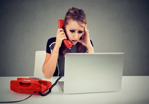 Stressé jeune femme malheureuse appelant sur un téléphone en regardant son ordinateur portable tout en étant assis à son bureau — Photo