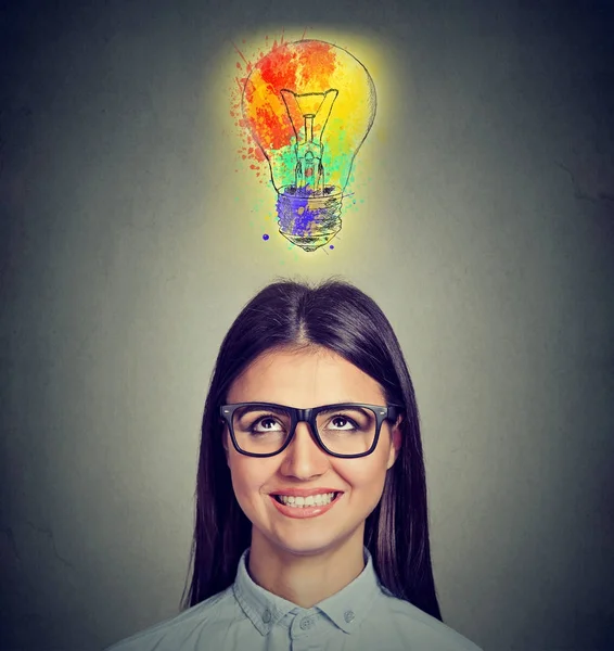 Portrait of a woman with glasses and creative idea looking up at colorful light bulb — Stock Photo, Image