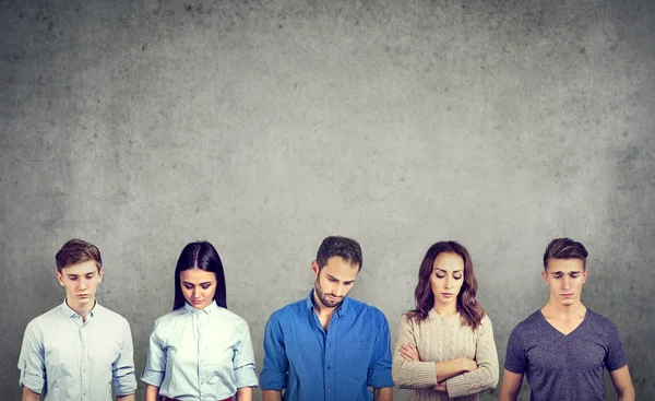Group of sad unhappy people men and women standing against gray wall looking down. — Stock Photo, Image