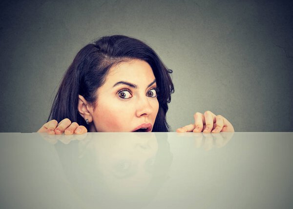 Surprised woman looking from behind table