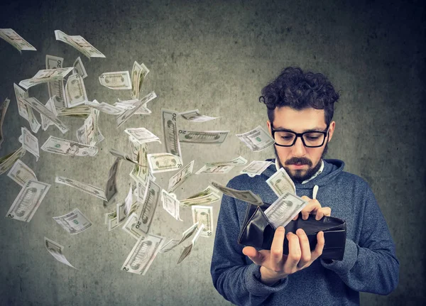 Hipster man looking at his wallet with money dollar banknotes flying out away — Stock Photo, Image