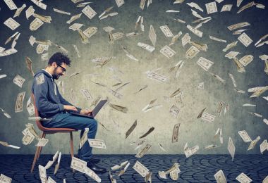 Online iş için fazladan para dolar altında bina bir dizüstü bilgisayar kullanan adam aşağı düşen nakit faturaları. 