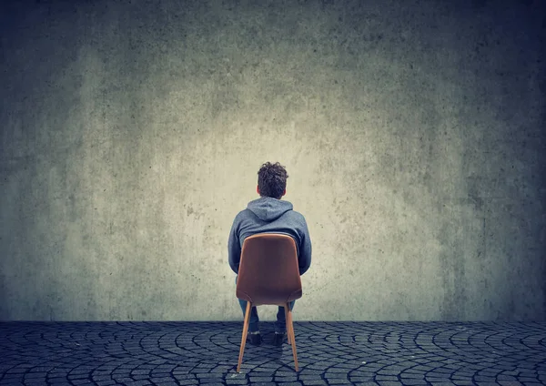 Ensam man på stol mot tom vägg — Stockfoto