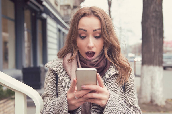 hocked anxious young girl looking at phone outdoors 