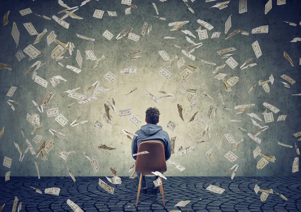 Az ember ül a szék előtt egy fal alatt a pénz eső — Stock Fotó