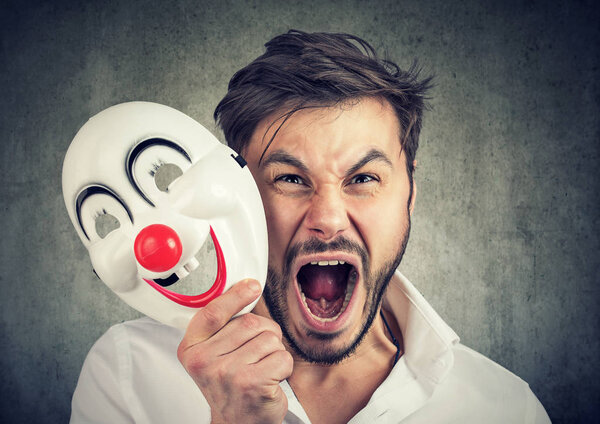 angry screaming man taking off a clown mask 
