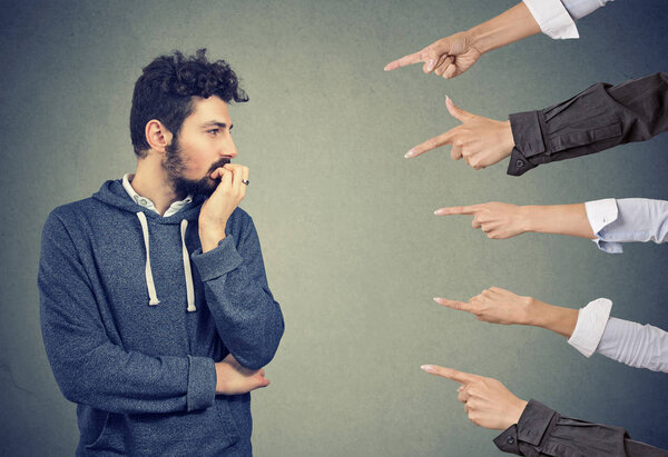 Anxious man judged by different people. Concept of accusation of guilty guy