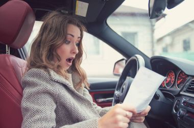 Shocked woman in car reading insurance paper clipart