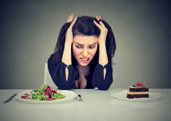 Страдающая девушка выбирает между тортом и салатом — стоковое фото