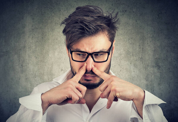 Человек щипает нос пальцами, смотрит с отвращением. Что-то воняет дурным запахом.
