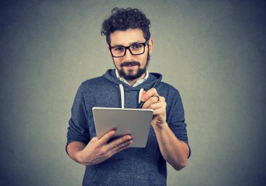Tablet bilgisayar ve kameraya bakarak kalem tutan bardaklarda Hispter adam