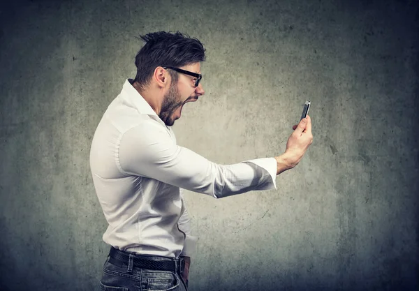 Wütender Mann hält Smartphone in der Hand und schreit vor Wut — Stockfoto