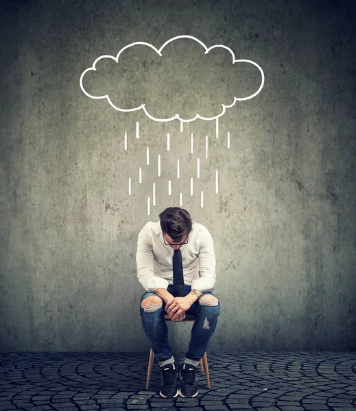 Smutny biznes człowiek siedzi na krześle, patrząc w dół z chmura deszcz nad nim — Zdjęcie stockowe