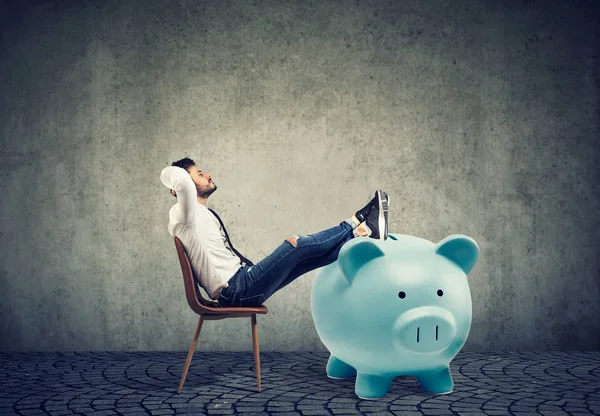 Jungunternehmer mit großem Sparschwein entspannt auf Stuhl sitzen — Stockbild Geschäftsmann mit großem Sparschwein entspannt auf Stuhl sitzen — Stockfoto