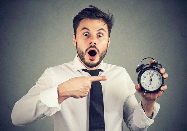 Scared man pointing at alarm clock