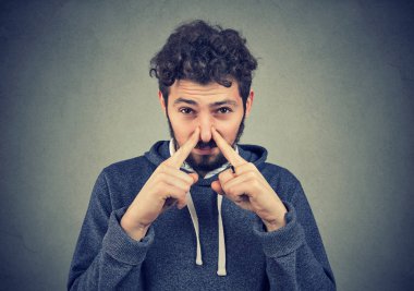 Kötü koku durum duvar arka plan üzerinde izole bir koku iğrenme ile tiksinti adam Pinch burun parmak ile görünüyor. İnsan yüzü ifade tepki