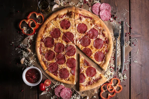 Pizza salami with cheese, salami, paprica and ketchup on dark wooden background