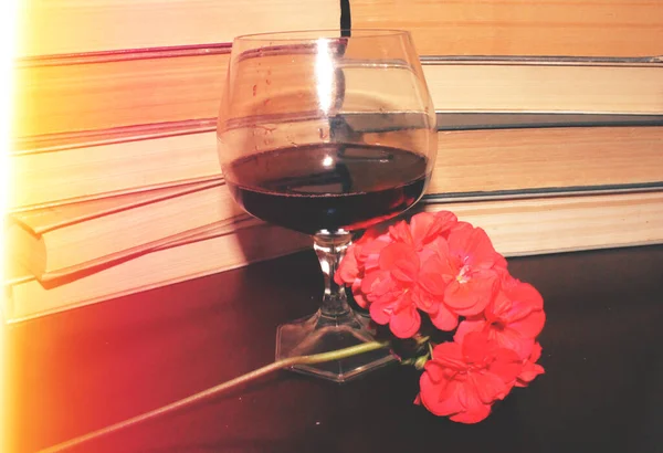 Kırmızı şarap kadehi ve kitaplar masanın üstünde.