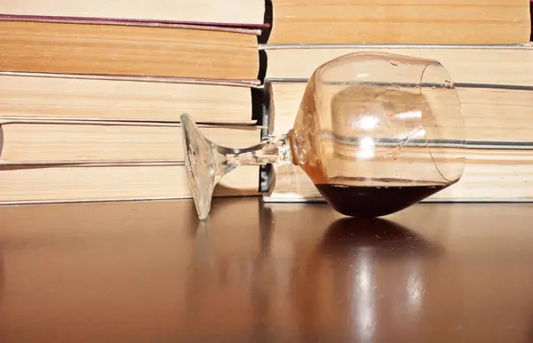 Kırmızı şarap kadehi ve kitaplar masanın üstünde.