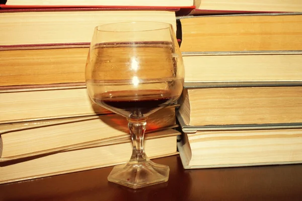 Kırmızı şarap kadehi ve kitaplar masanın üstünde.