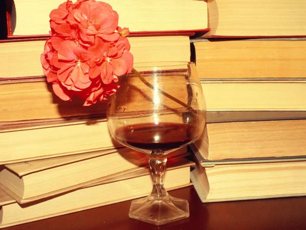 Kırmızı şarap kadehi ve kitaplar masanın üstünde.