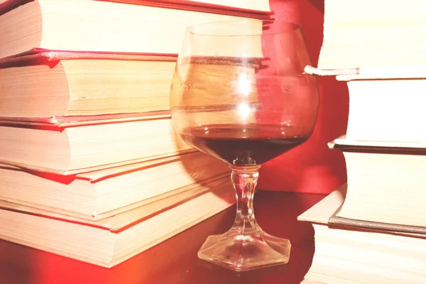 Kırmızı şarap kadehi ve kitaplar masanın üstünde.