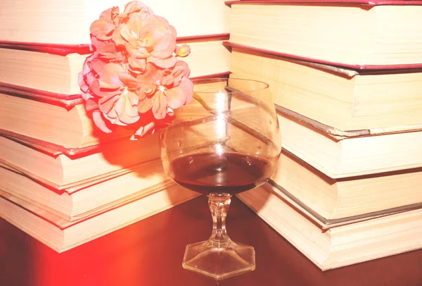 Kırmızı şarap kadehi ve kitaplar masanın üstünde.