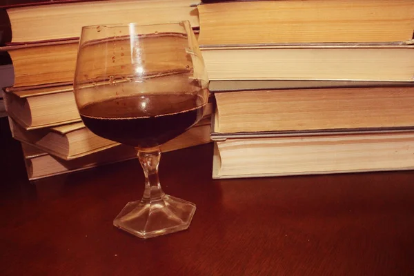 Kırmızı şarap kadehi ve kitaplar masanın üstünde.