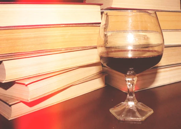 Kırmızı şarap kadehi ve kitaplar masanın üstünde.