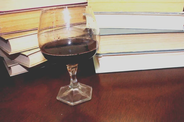 Kırmızı şarap kadehi ve kitaplar masanın üstünde.