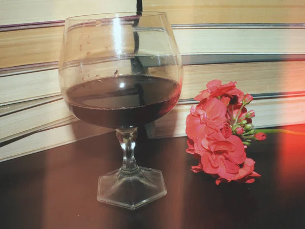 Kırmızı şarap kadehi ve kitaplar masanın üstünde.