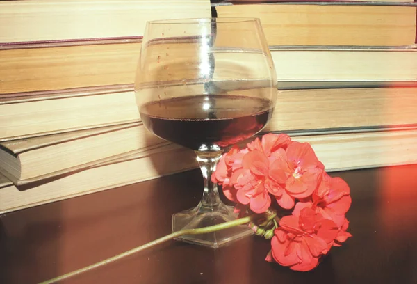 Kırmızı şarap kadehi ve kitaplar masanın üstünde.